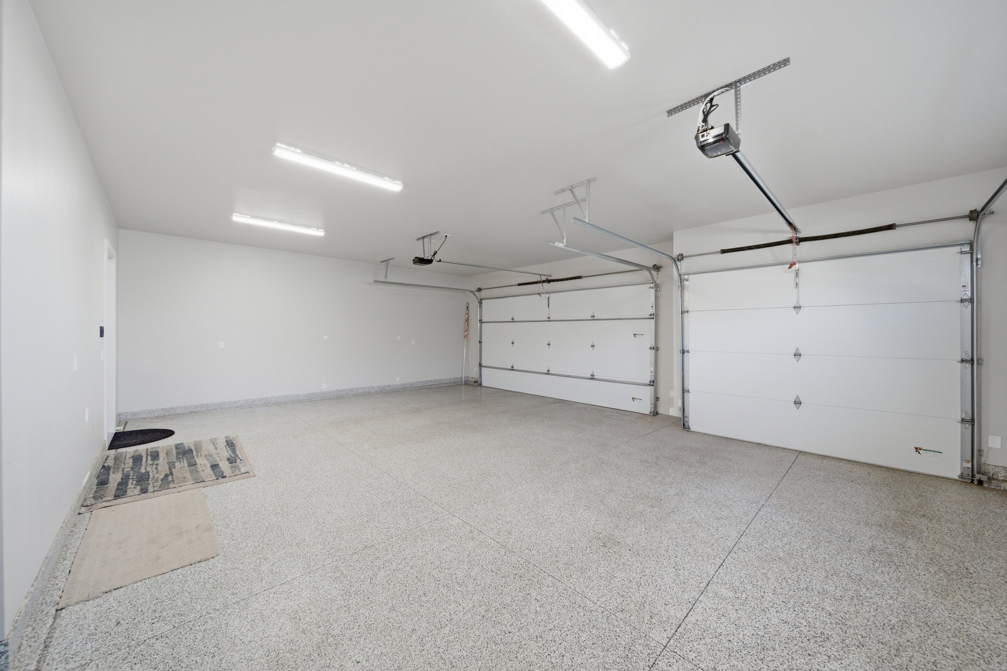 Spacious garage featuring two overhead doors, automatic openers, epoxy flooring, and ample overhead lighting