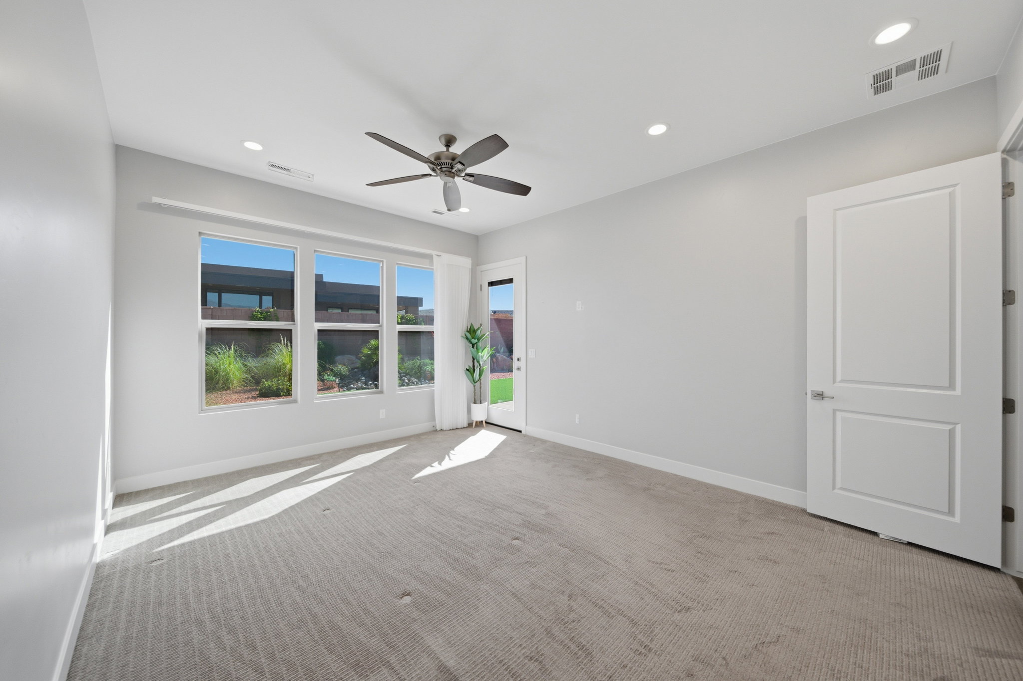 Carpeted interior space featuring a ceiling fan, recessed lighting, multiple windows, and a glass-paneled door
