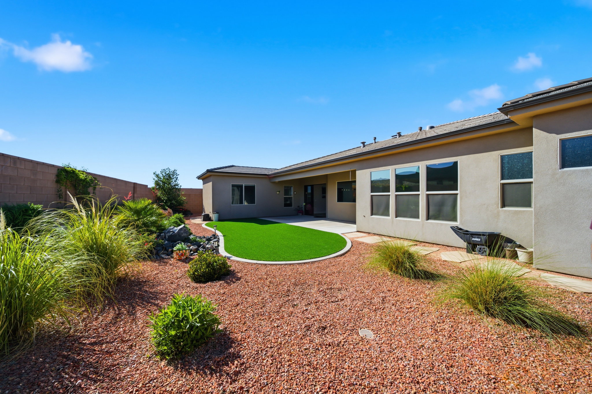 Spacious backyard featuring an artificial turf lawn, a concrete patio, and desert landscaping with decorative rock and various plantings