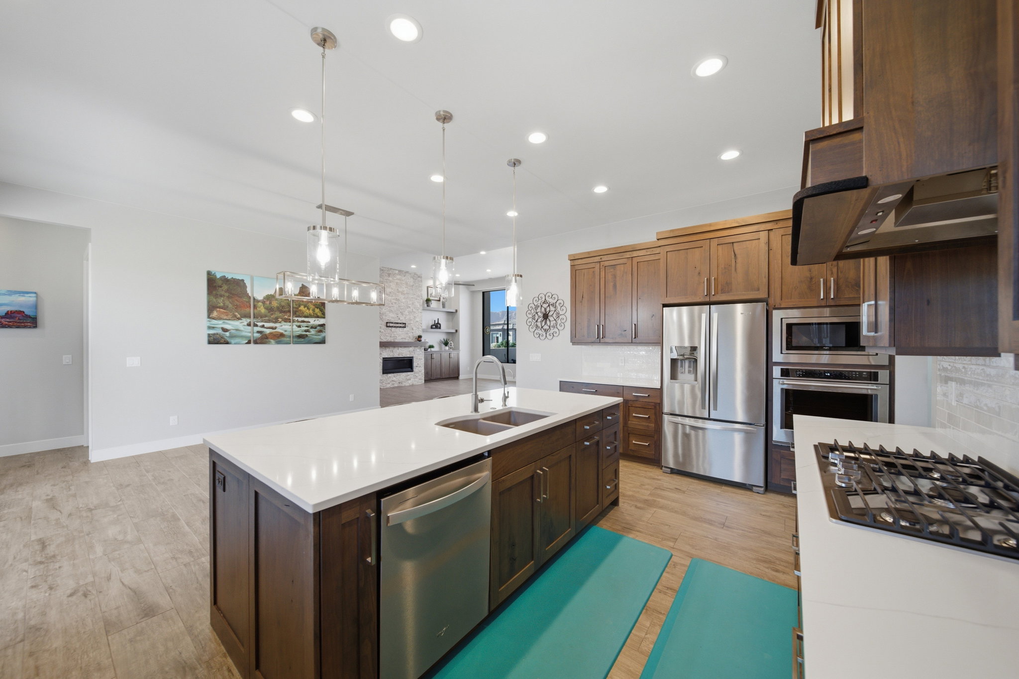 Expansive kitchen featuring a large island with a dual-basin sink, quartz countertops, stainless steel appliances, wood-finish cabinetry, and recessed lighting