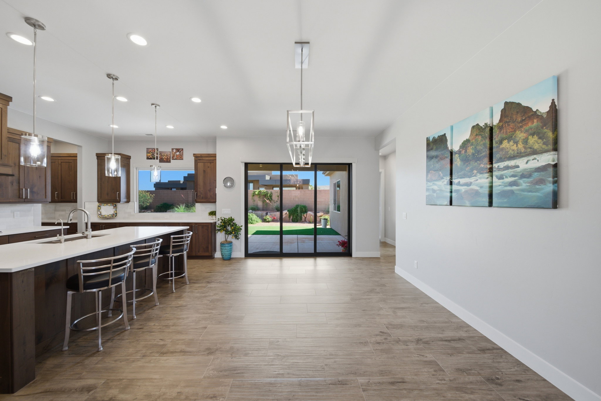 Open concept living area featuring wood-finish flooring, a kitchen island with seating, a sliding glass door to the backyard, recessed lighting, and pendant light fixtures