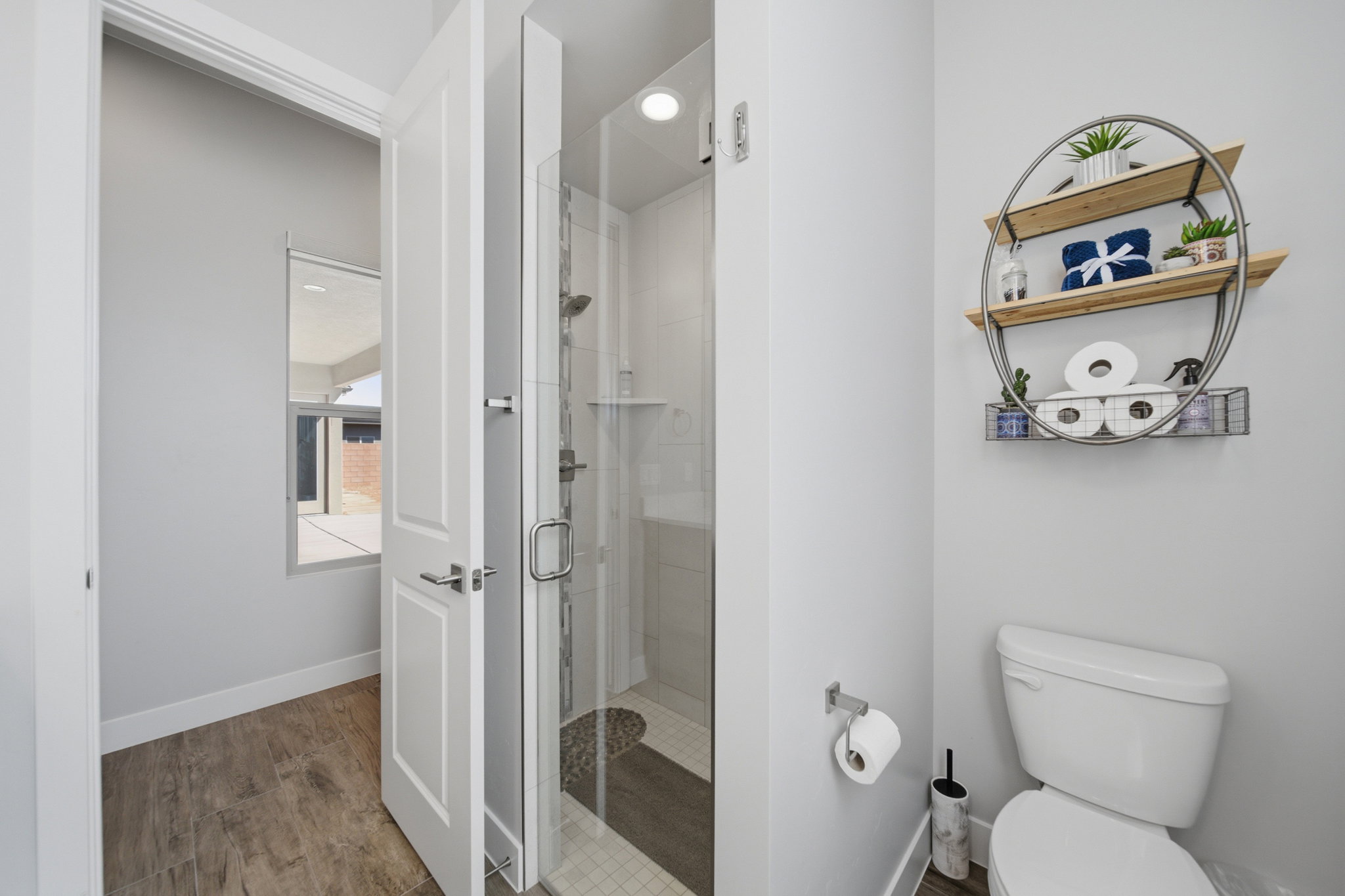 Bathroom featuring a glass-enclosed shower with a pebble-style floor, wood-finish flooring, and a window
