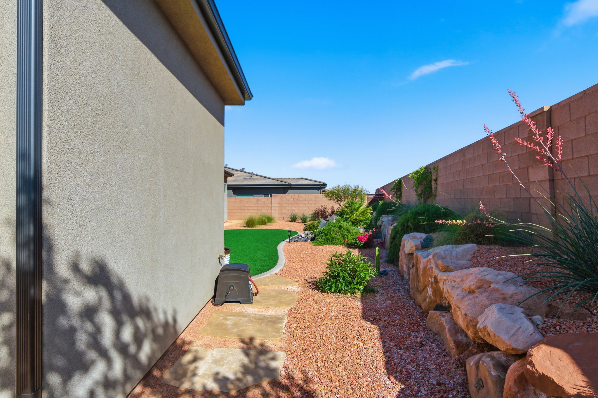 Landscaped exterior featuring a stucco facade, dark gutters, a block wall perimeter, and a rock garden with varied plantings