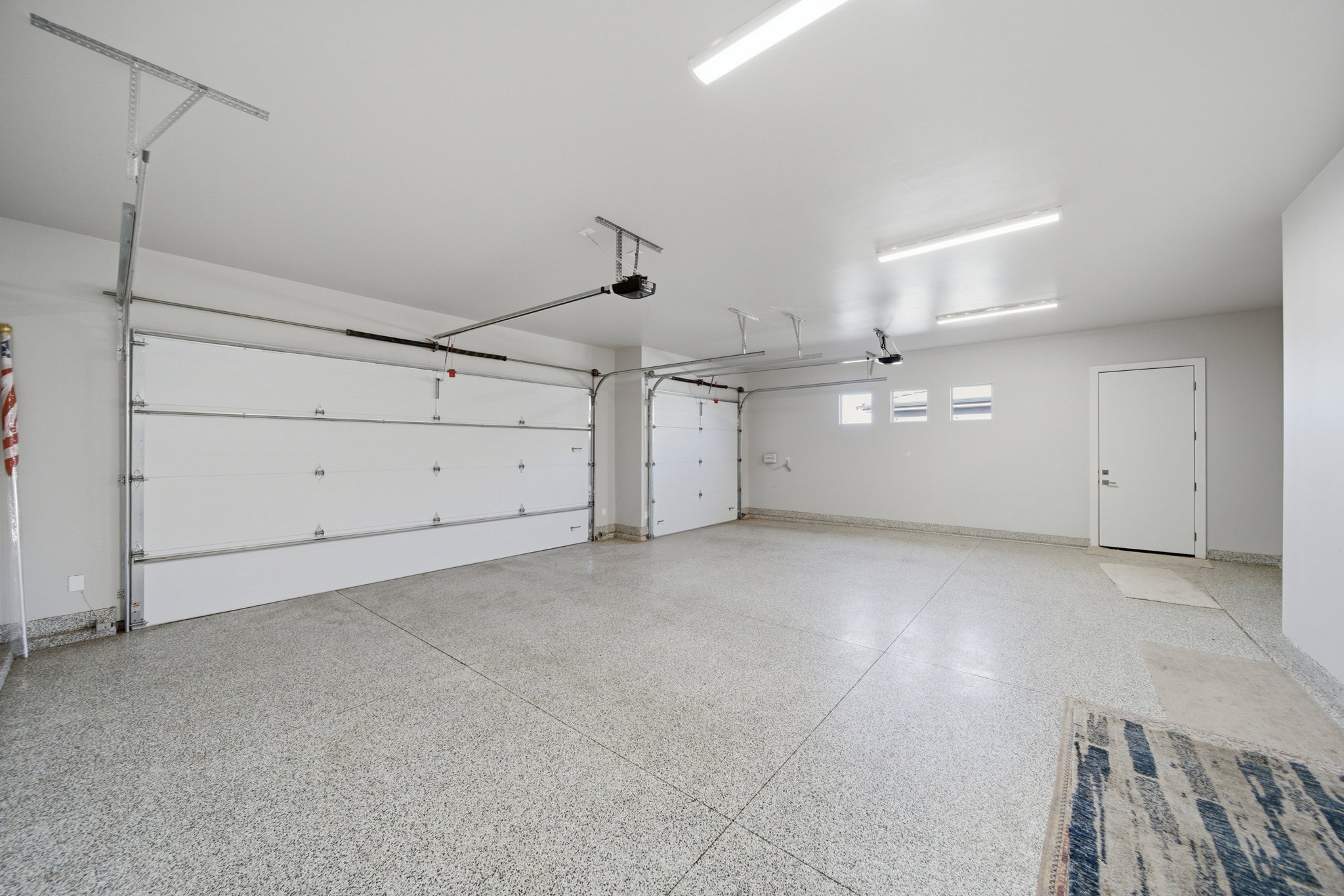Spacious garage featuring a durable epoxy floor, white sectional garage doors, and multiple ceiling-mounted light fixtures