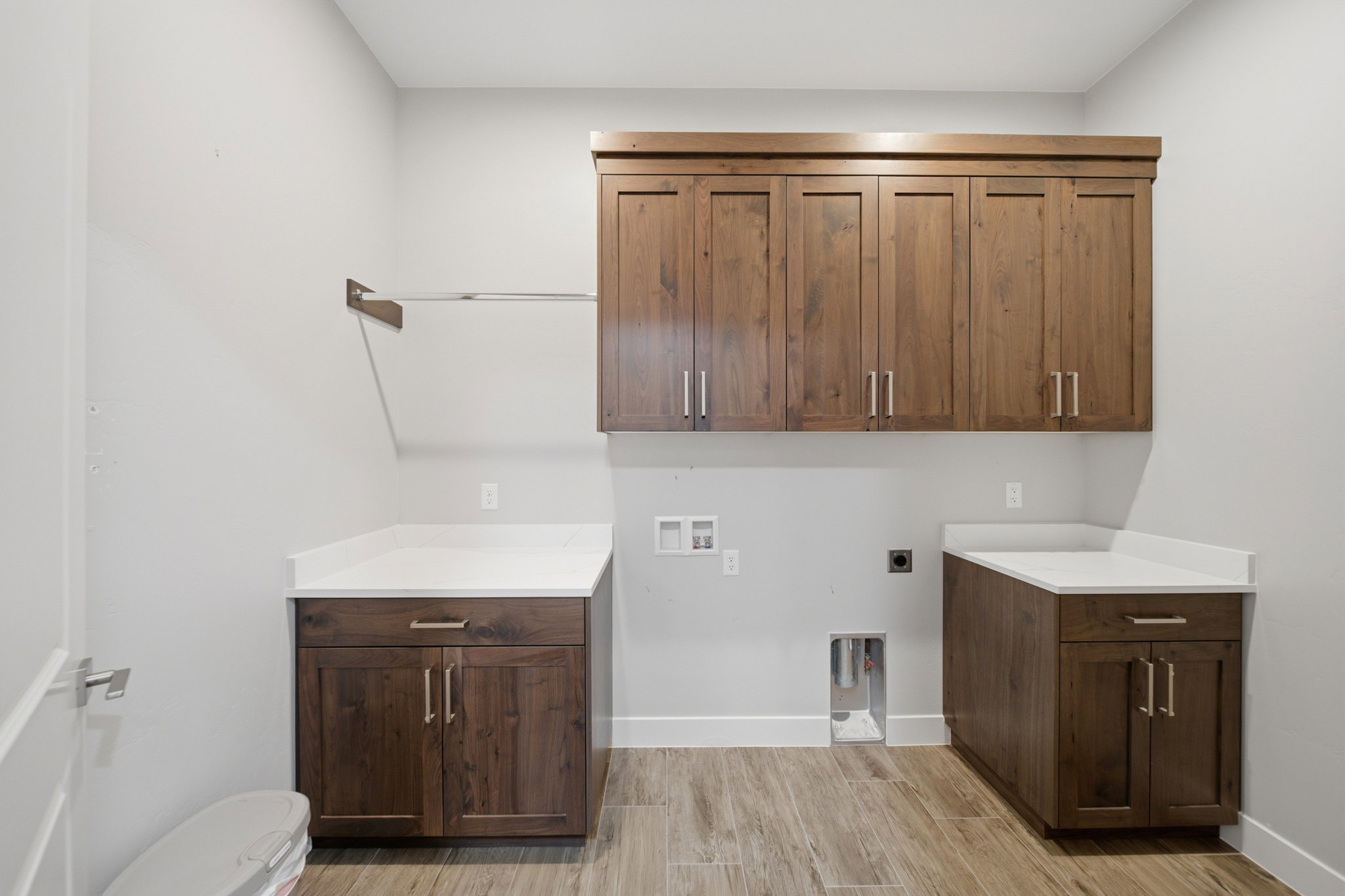Dedicated laundry space featuring extensive custom wood cabinetry, clean white countertops, and wood-finish flooring
