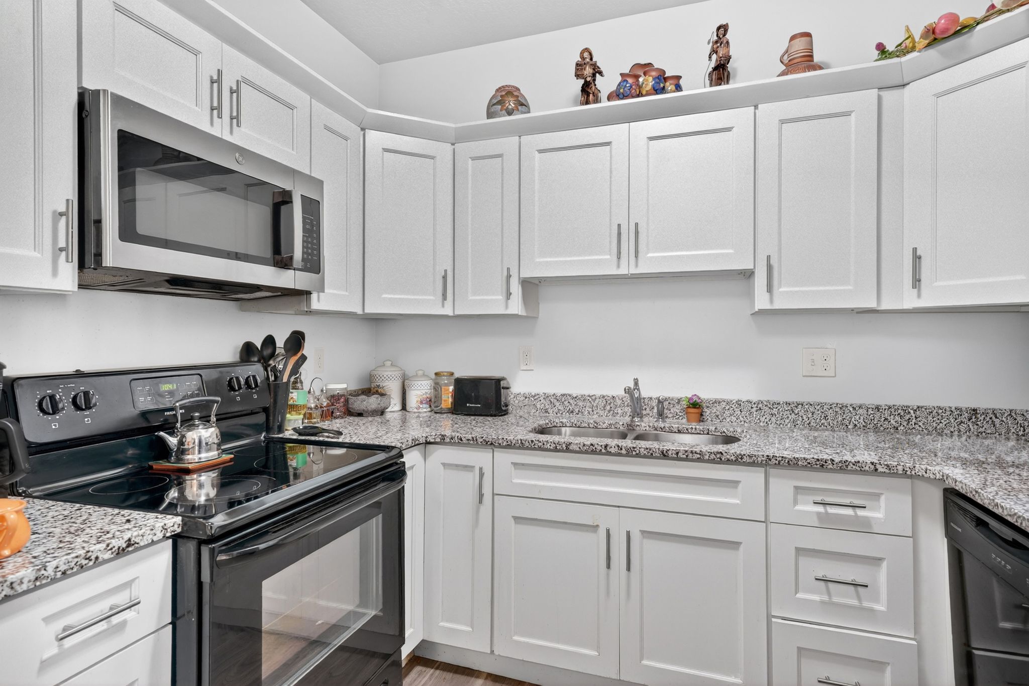 Kitchen featuring white shaker-style cabinetry, a stainless steel over-the-range microwave, granite countertops, and a double basin stainless steel sink