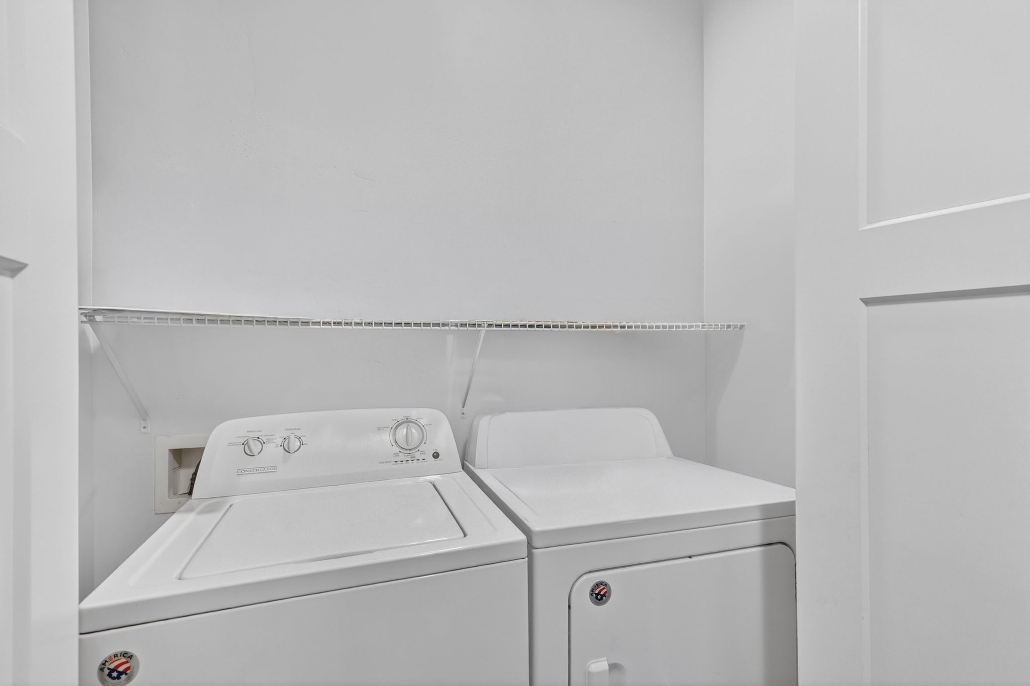 Dedicated laundry area featuring a white top-load washing machine, a white front-load dryer, and a wire storage shelf