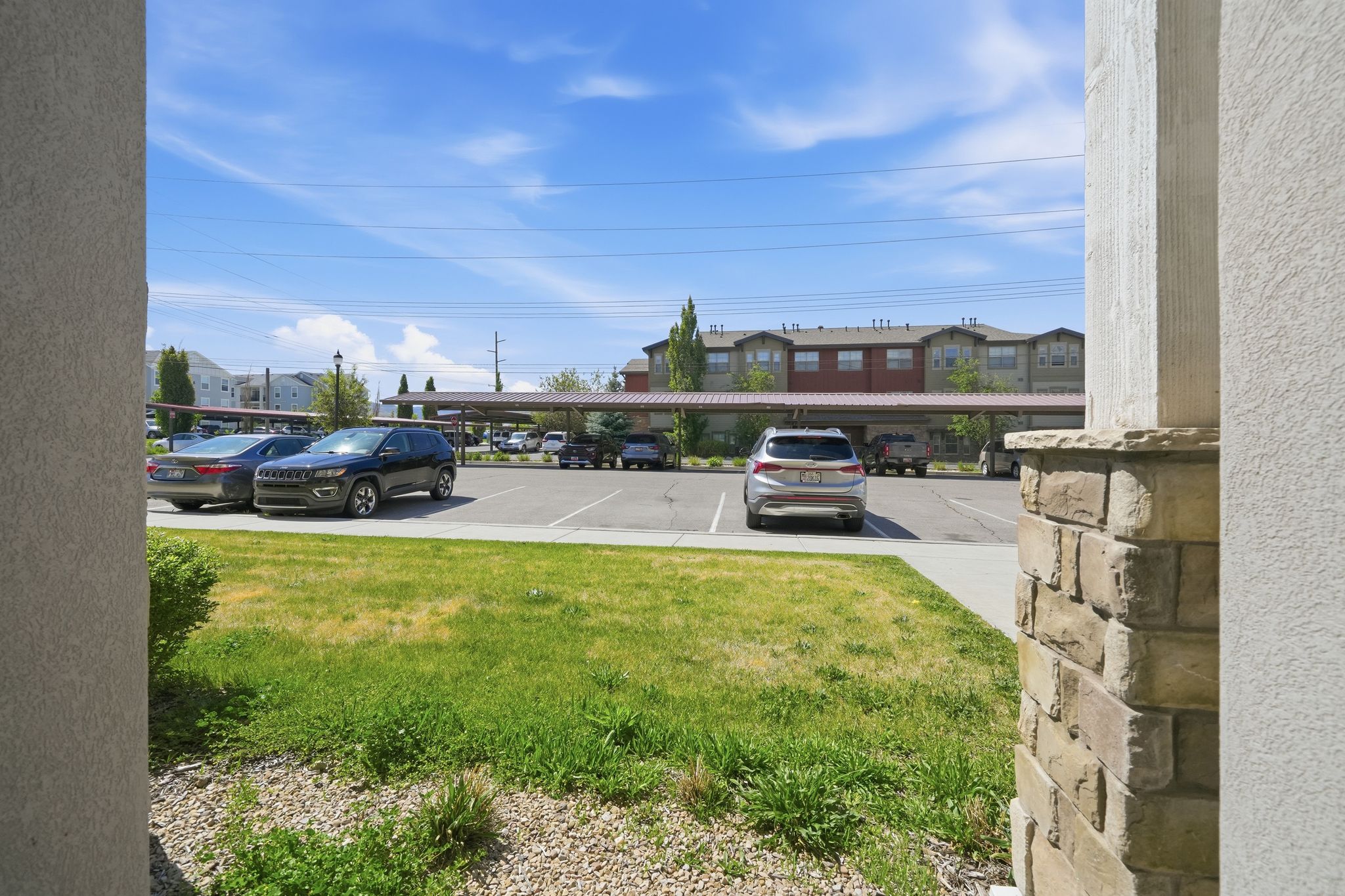 Landscaped grounds with a stone-accented pillar, leading to a parking area with covered spaces