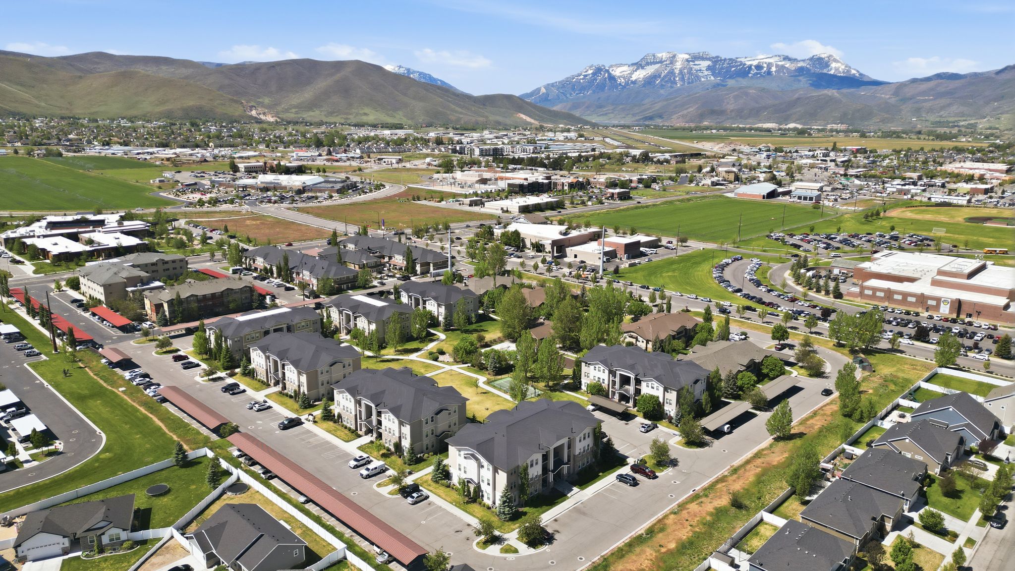 Expansive aerial showcasing a residential community with multi-story buildings, covered parking areas, and green spaces