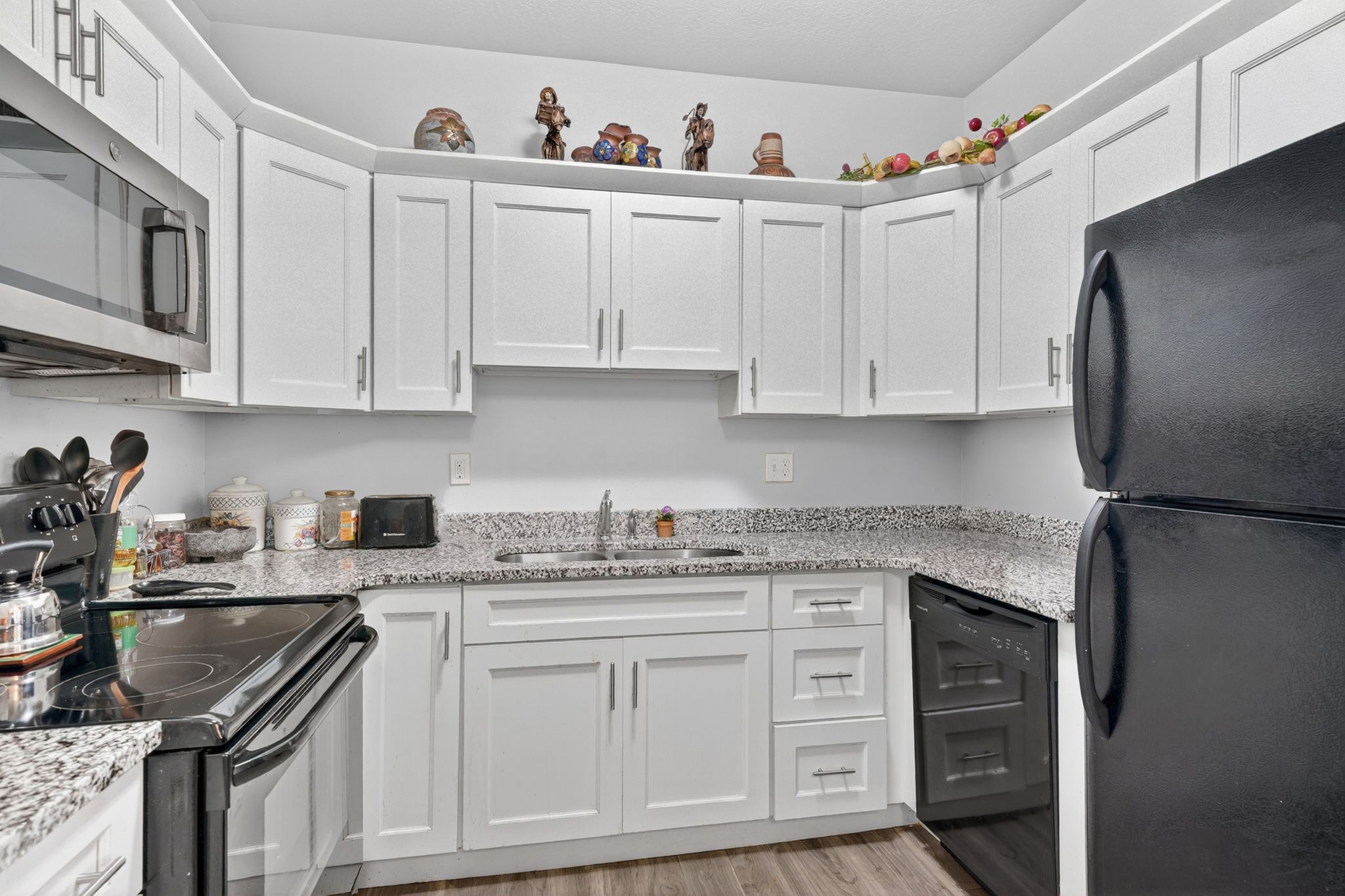Modern kitchen featuring white shaker cabinetry, granite-style countertops, stainless steel microwave, black electric range, and black refrigerator