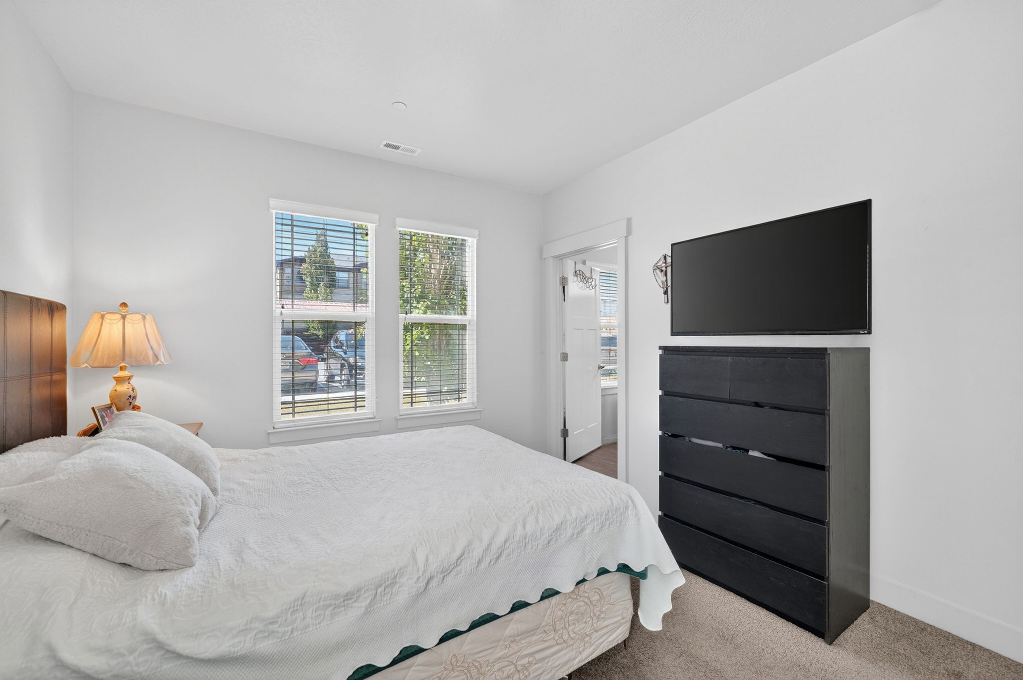 Bedroom featuring two windows with blinds, a wood-finish headboard, and light-toned carpeting