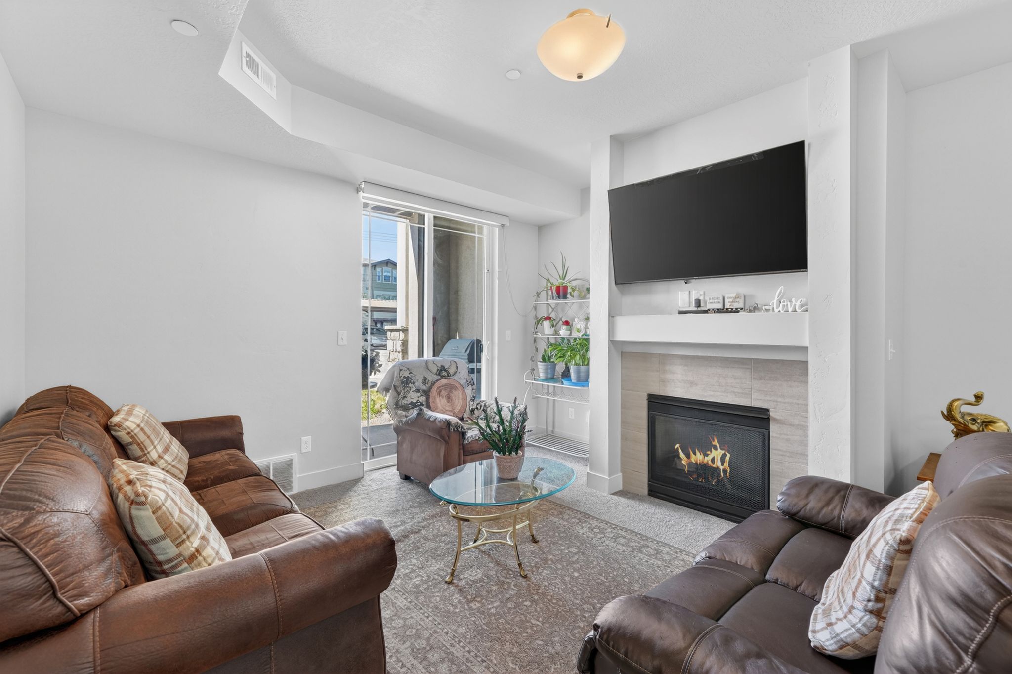 Living area featuring a gas fireplace with a tiled surround and mantel, sliding glass doors, carpet flooring, and a ceiling-mounted light fixture