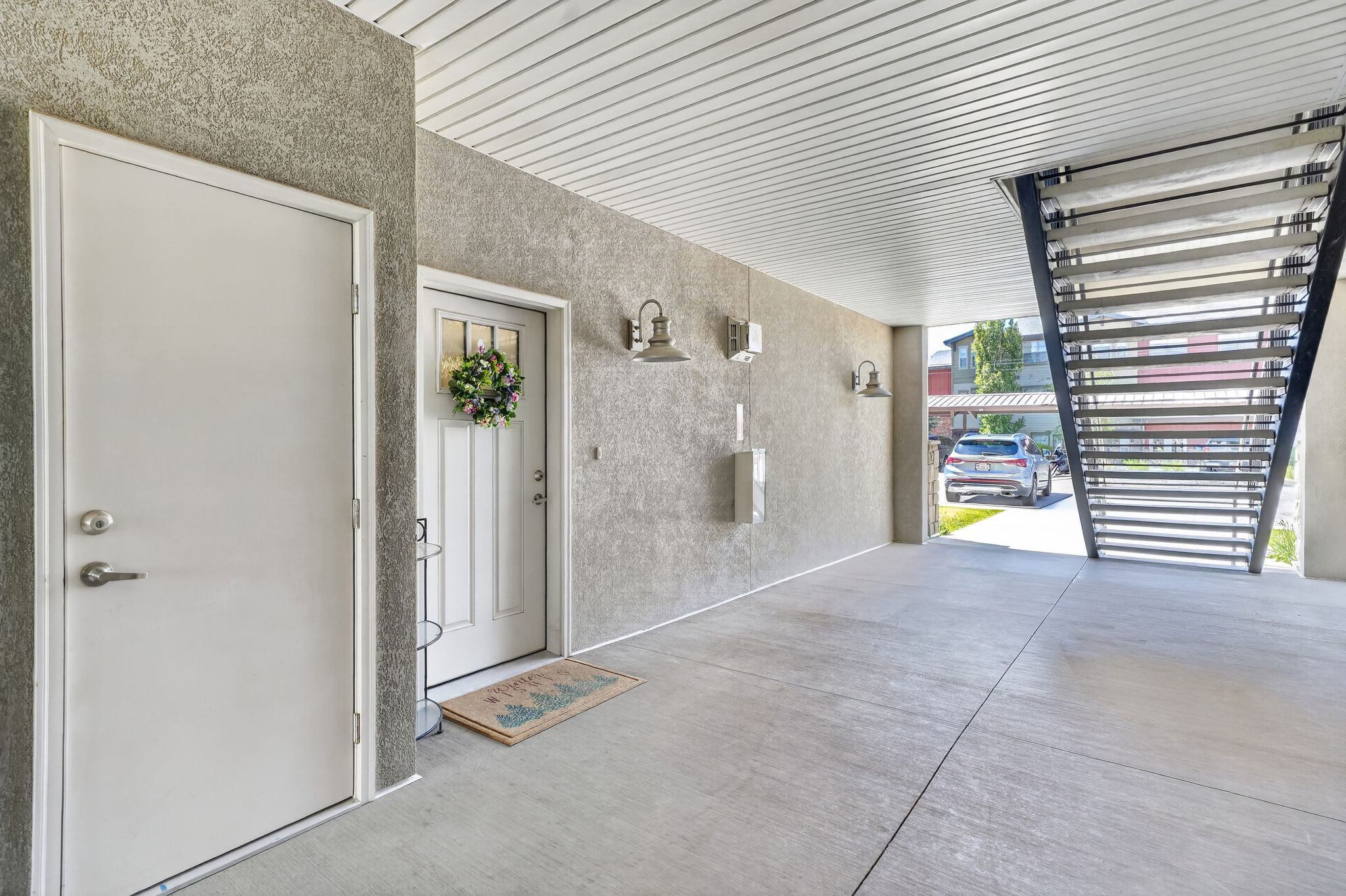 Covered entry area featuring textured gray walls, concrete flooring, a white paneled door with glass inserts, and a second white entry door