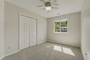 Neutral-toned room featuring a window with natural scenery, light gray carpeting, and a ceiling fan with integrated lighting