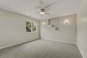 Spacious room featuring neutral carpet, a ceiling fan with integrated lighting, recessed wall niche, and modern sconce lighting