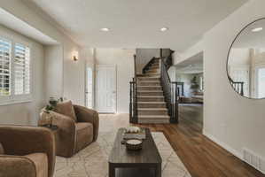 Hardwood-style flooring extends through the entry and into a carpeted staircase with dark wood railings