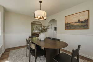 Dining area featuring wood-finish flooring, a contemporary drum pendant light fixture, and arched doorways