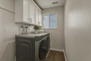 Dedicated laundry space featuring white upper cabinetry with brushed nickel hardware, a window, wood-finish flooring, and light gray walls