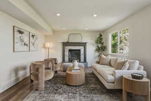 Living area featuring a stone-clad fireplace with a dark wood mantel, recessed lighting, wood-finish flooring, and a large window