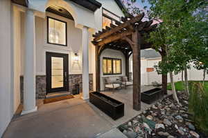 Inviting entry featuring a covered porch, stone accent wall, and a dark wood pergola