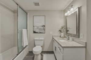 Bathroom featuring a white vanity with a light-toned countertop, a framed mirror with an overhead light fixture, a shower-over-tub combination with a sliding glass door, and dark tile flooring