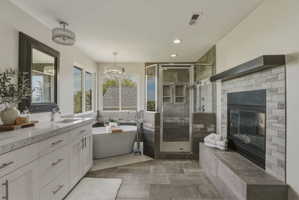 Bathroom featuring a freestanding tub, glass-enclosed shower, dual vanity with undermount sinks, tile surround fireplace, and large format floor tiling
