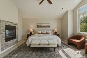 Spacious bedroom featuring an integrated fireplace with stone-look tile surround, large window, ceiling fan, and high ceilings