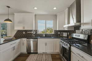 Kitchen featuring white shaker cabinetry, dark subway tile backsplash, dark countertops, and stainless steel appliances