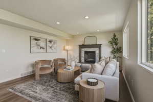 Living area featuring recessed lighting, wood-finish flooring, and a fireplace with a stone surround and dark mantle