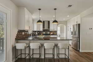 Open-concept kitchen featuring white cabinetry, dark stone countertops, stainless steel appliances, and wood-finish flooring