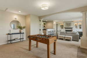 Spacious entertainment area with neutral carpeting and a built-in wet bar featuring a countertop with barstool seating