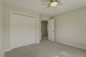 Carpeted room featuring a built-in bi-fold closet, neutral wall paint, white trim, and a ceiling fan with integrated lighting