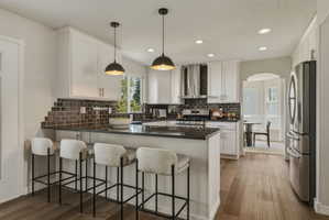 Contemporary kitchen featuring an island with counter seating, a dark tile backsplash, stainless steel appliances, and wood-finish flooring
