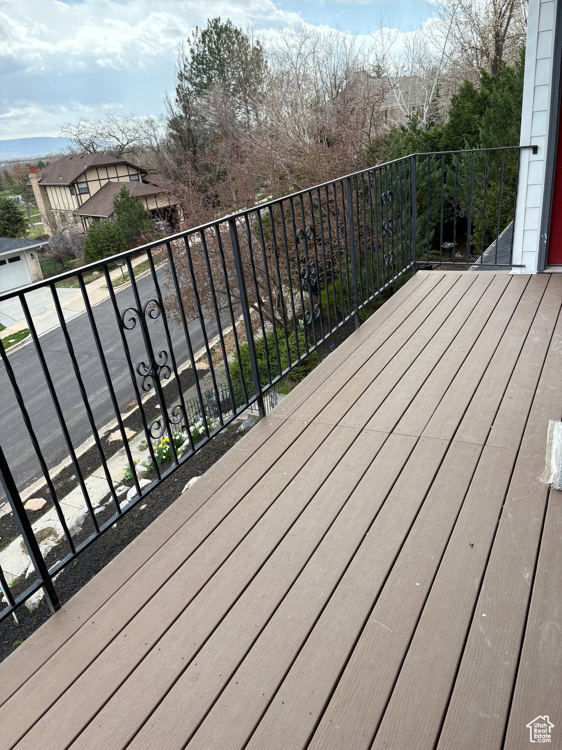 Outdoor balcony featuring composite decking, black wrought iron railing, and a red entry door