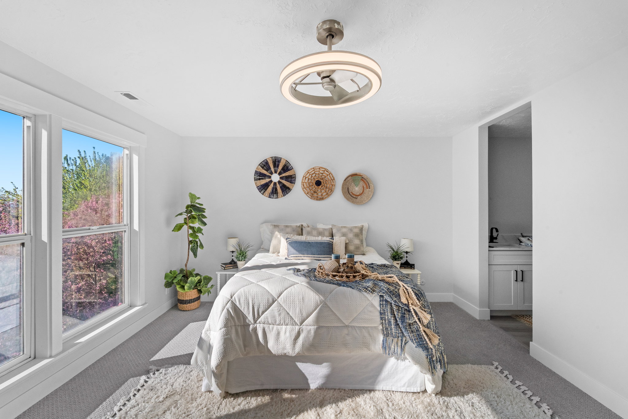 Bright bedroom featuring two large windows, a modern ceiling fan with integrated lighting, and neutral carpeting