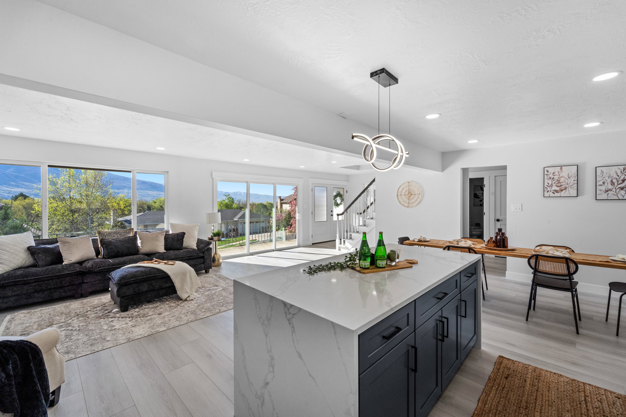 Open-concept living area featuring an expansive kitchen island with a waterfall countertop, contemporary pendant lighting, large windows, and sliding glass doors