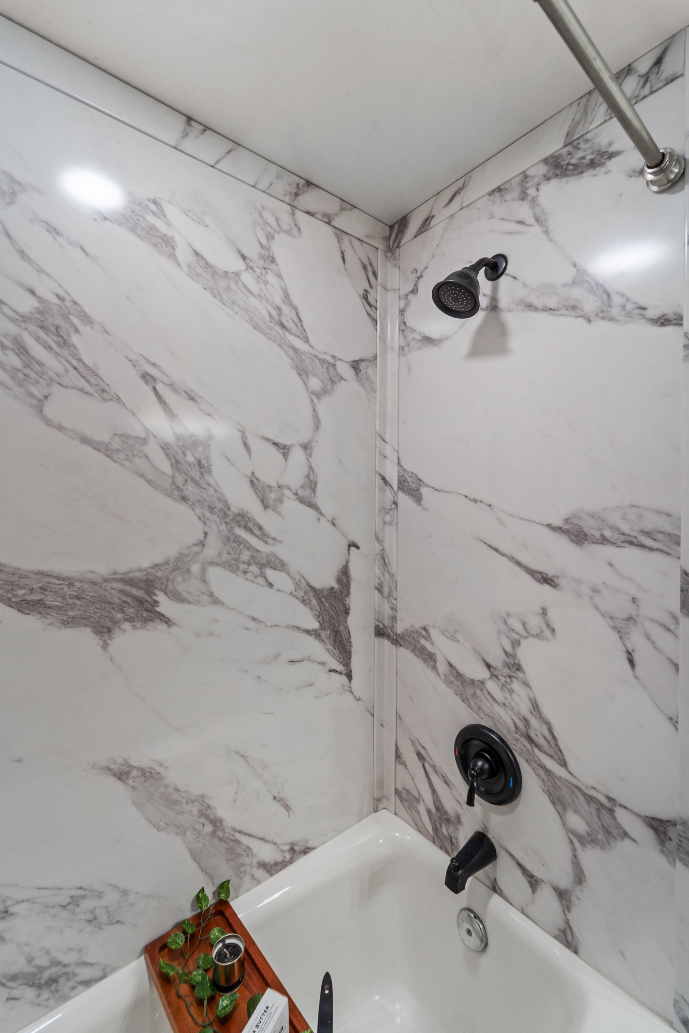Tub and shower combination featuring marble-patterned wall surrounds, a matte black showerhead, and a matching matte black tub filler with a single-handle control