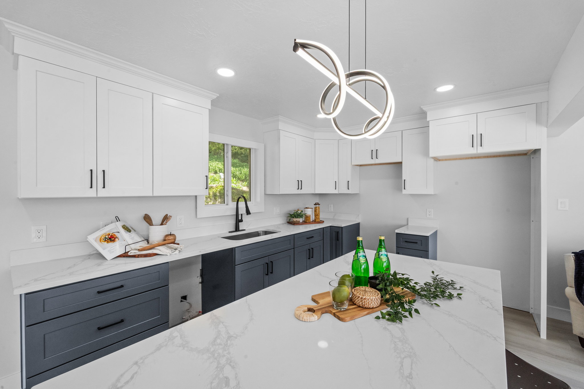 Contemporary kitchen featuring a large central island with a waterfall edge, white shaker-style upper cabinetry, dark base cabinetry, quartz countertops, and a modern pendant light fixture