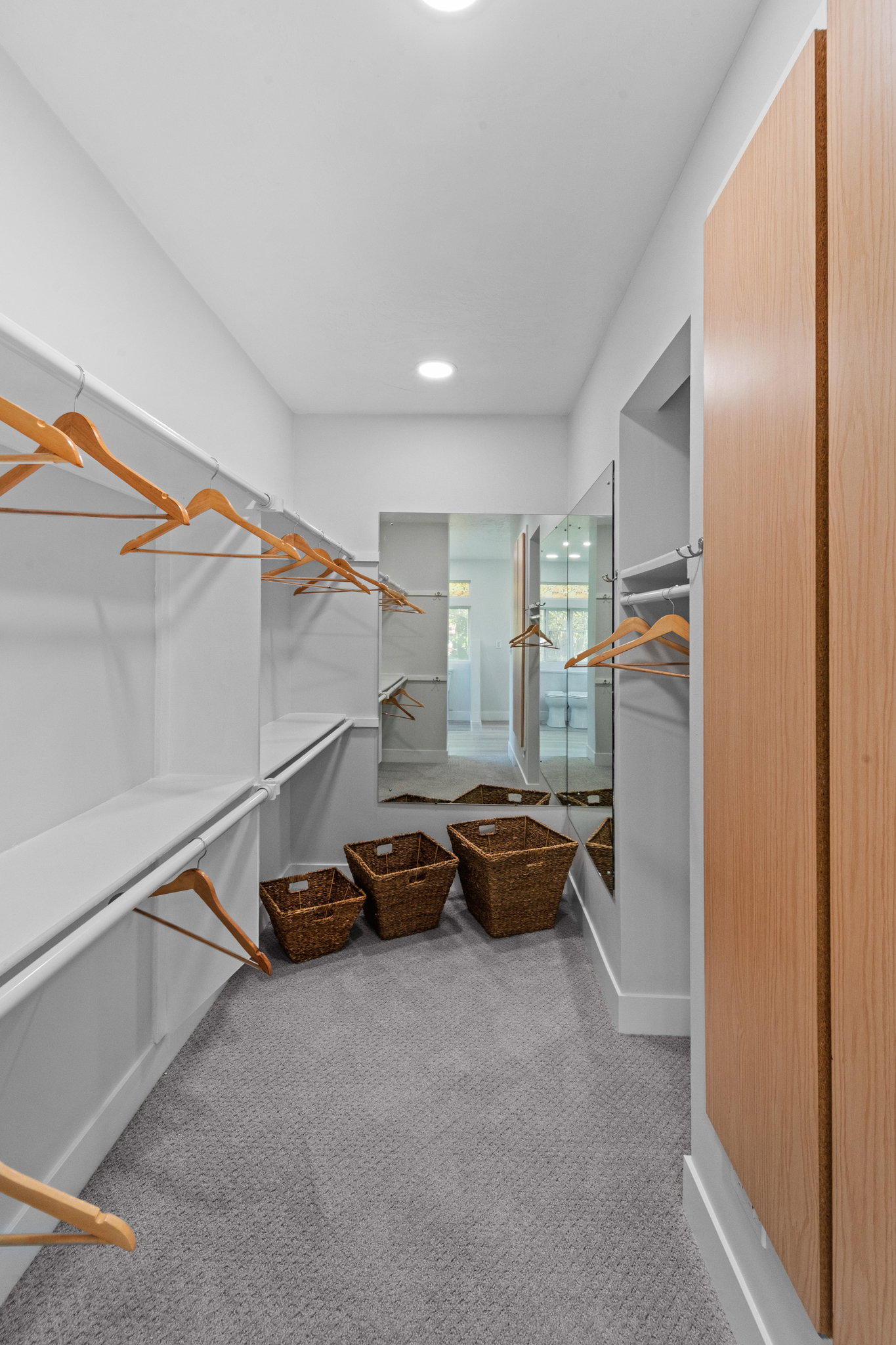 Walk-in closet featuring extensive built-in shelving, hanging rods, recessed ceiling lighting, and light wood-finish cabinetry