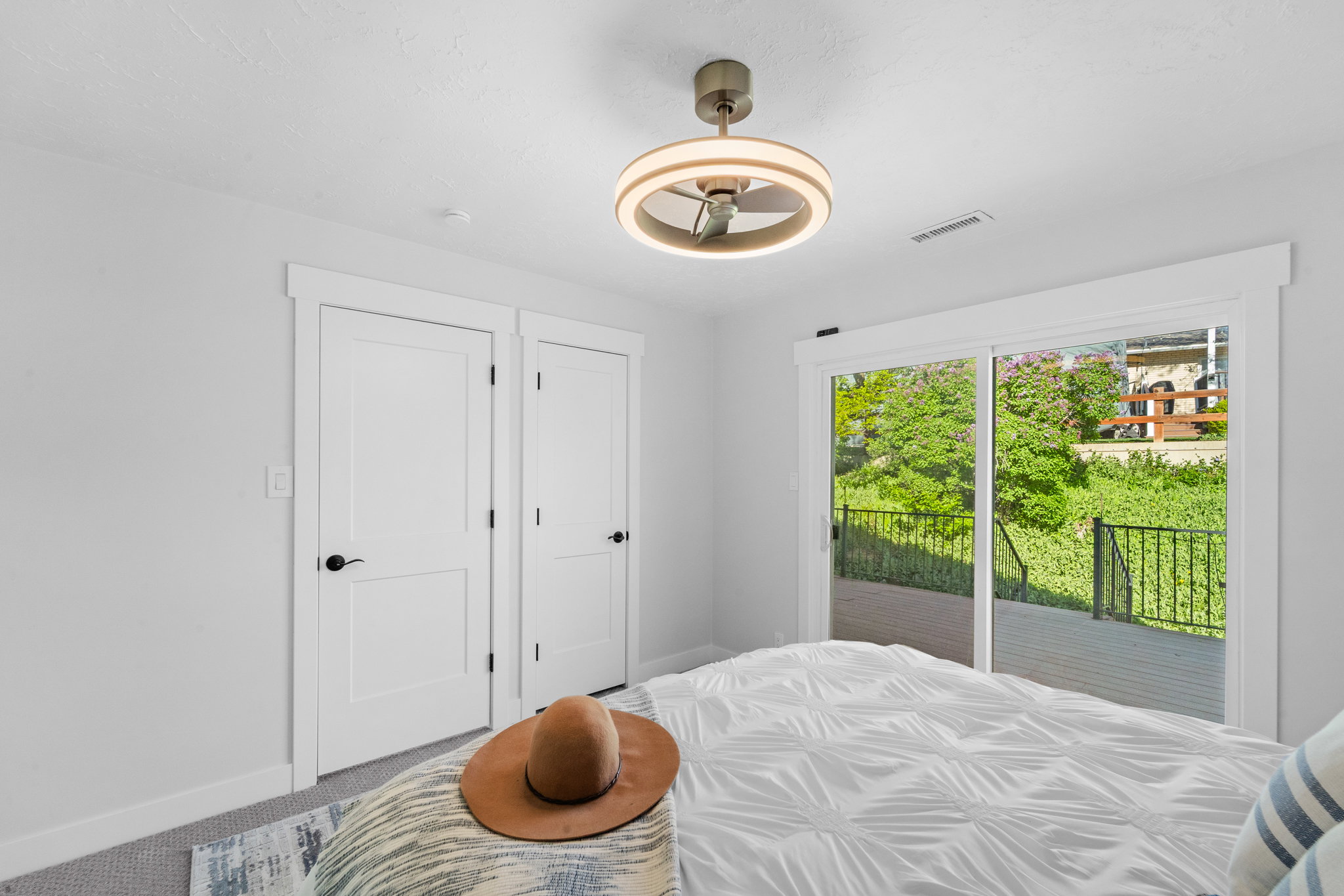 Sliding glass door opening to a private deck with black metal railing, offering lush green outdoor scenery