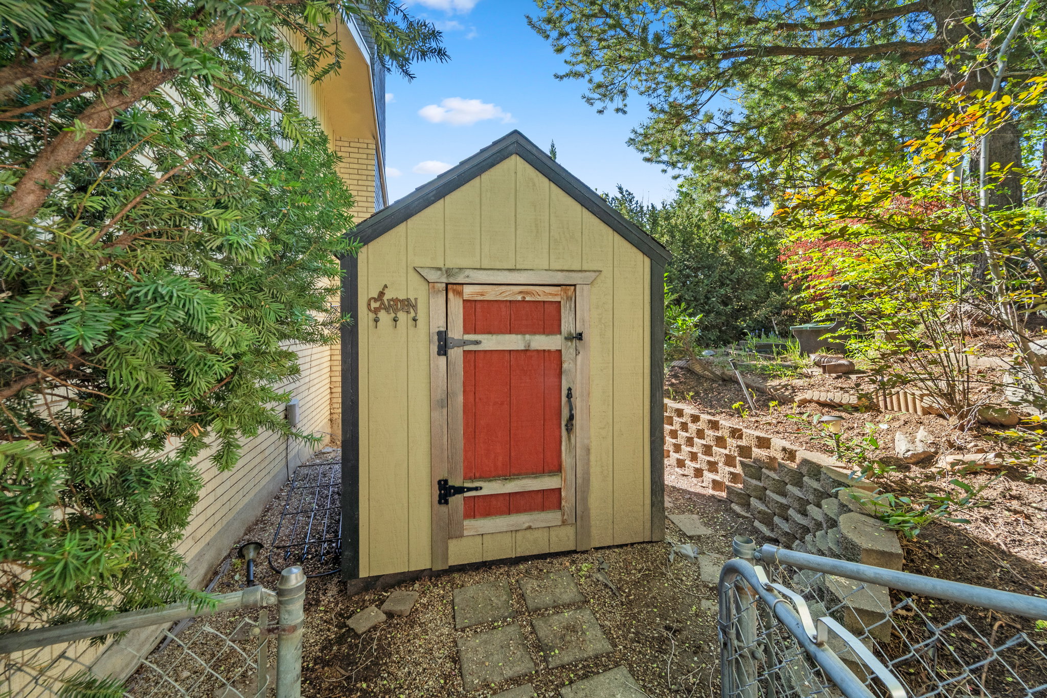 Gabled storage shed with a vibrant red door, featuring a shingle roof and light-colored siding