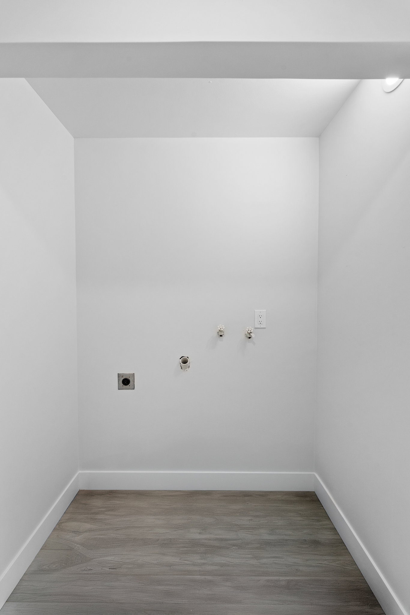 Dedicated utility space featuring light wood-finish flooring and crisp white baseboards