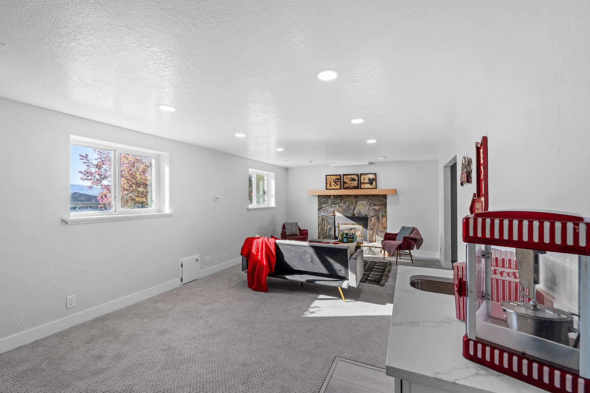 Spacious recreation room featuring recessed lighting, gray carpeting, and a stone-faced fireplace with a wood mantel