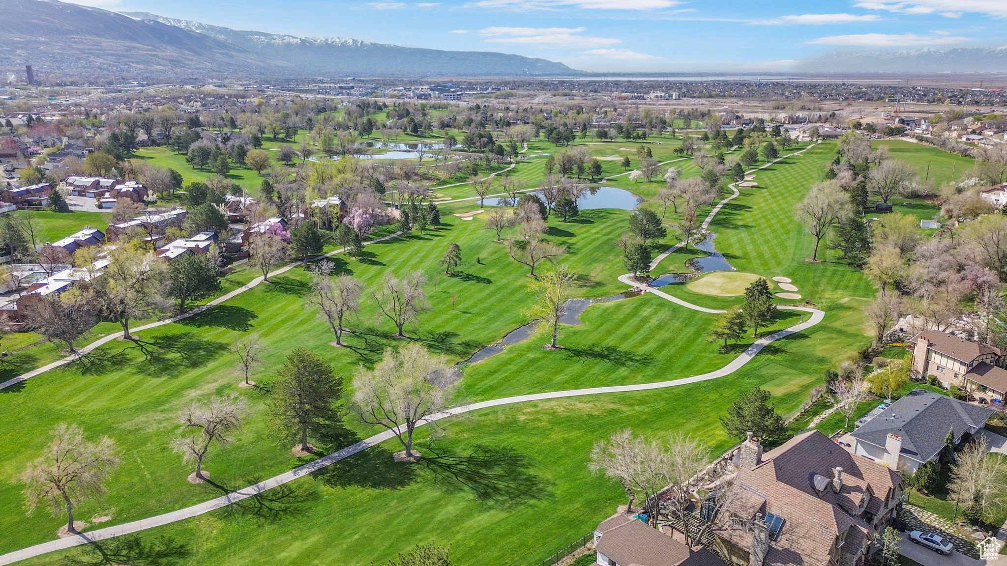 Expansive golf course setting featuring manicured fairways, mature trees, multiple water features, and mountain backdrops
