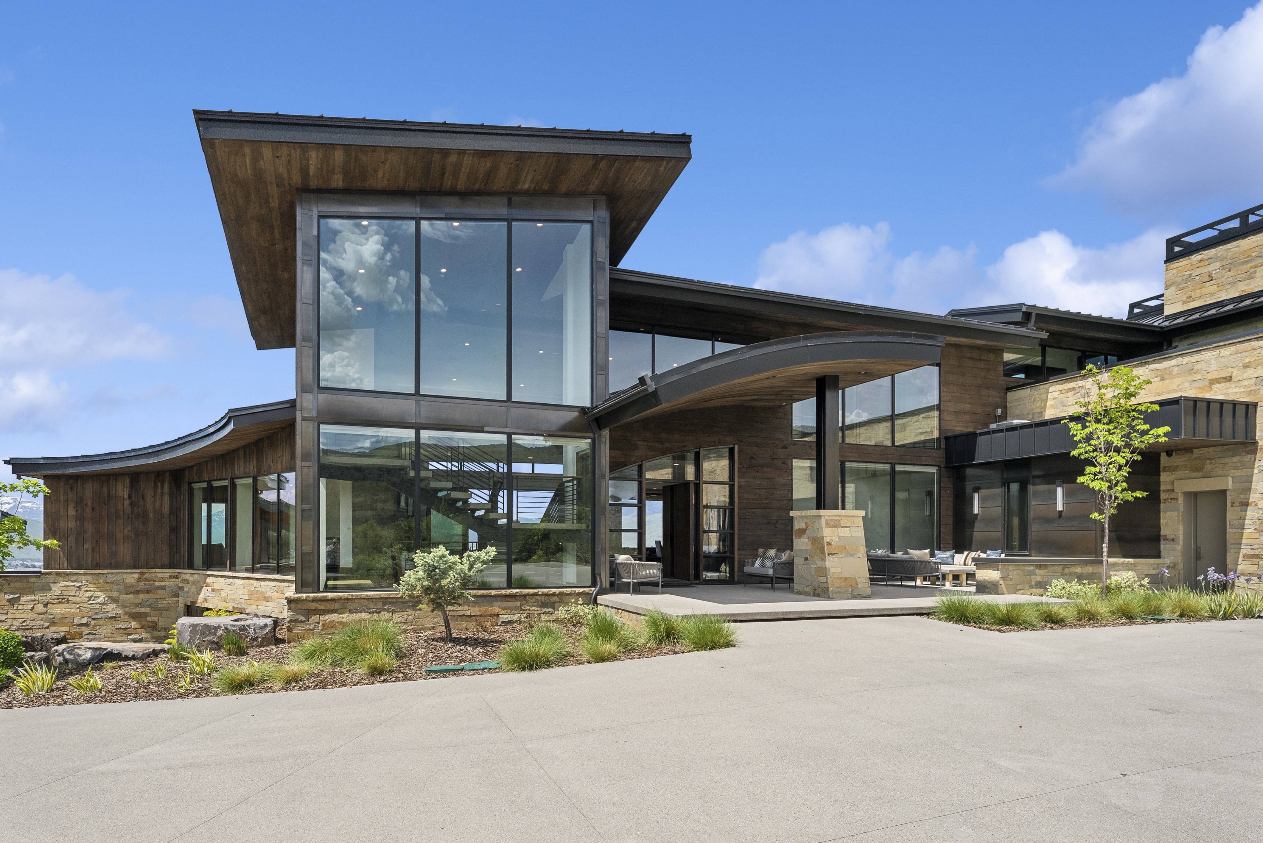 Contemporary architectural design featuring extensive window walls, stacked stone accents, rich wood paneling, and a curved roofline