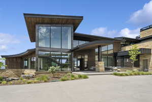 Contemporary architectural design featuring extensive window walls, stacked stone accents, rich wood paneling, and a curved roofline