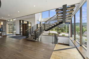 Floating staircase with open risers and metal railing, expansive window wall, wood-finish flooring, recessed lighting, and a modern entryway with glass paneling