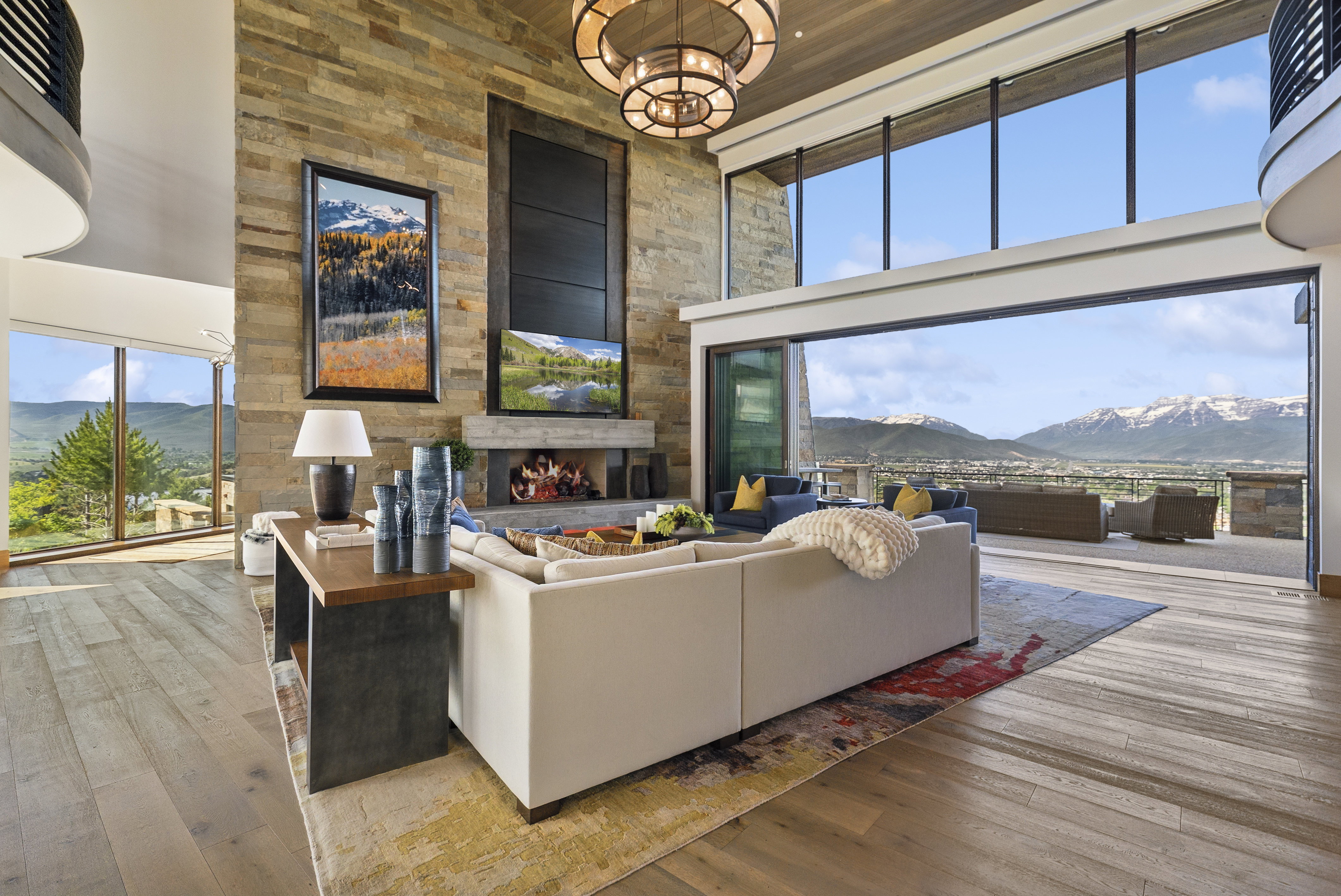 Spacious great room featuring a floor-to-ceiling stone fireplace, high ceilings, large format wood-finish flooring, and expansive sliding glass doors opening to the outdoor living area