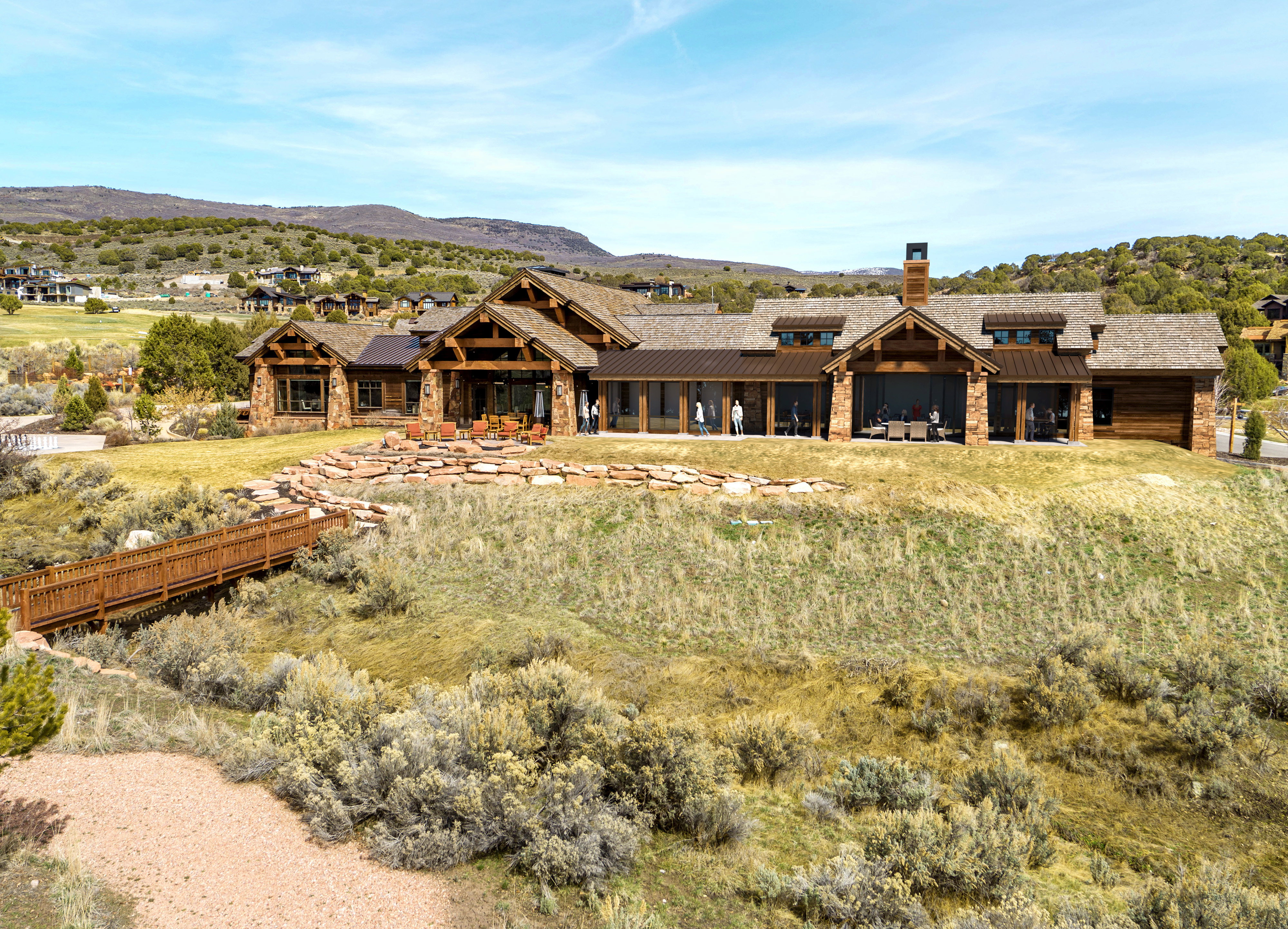 Expansive property featuring a stone and wood exterior with a prominent chimney, multiple gabled roofs, a broad outdoor patio, and a rustic wooden bridge