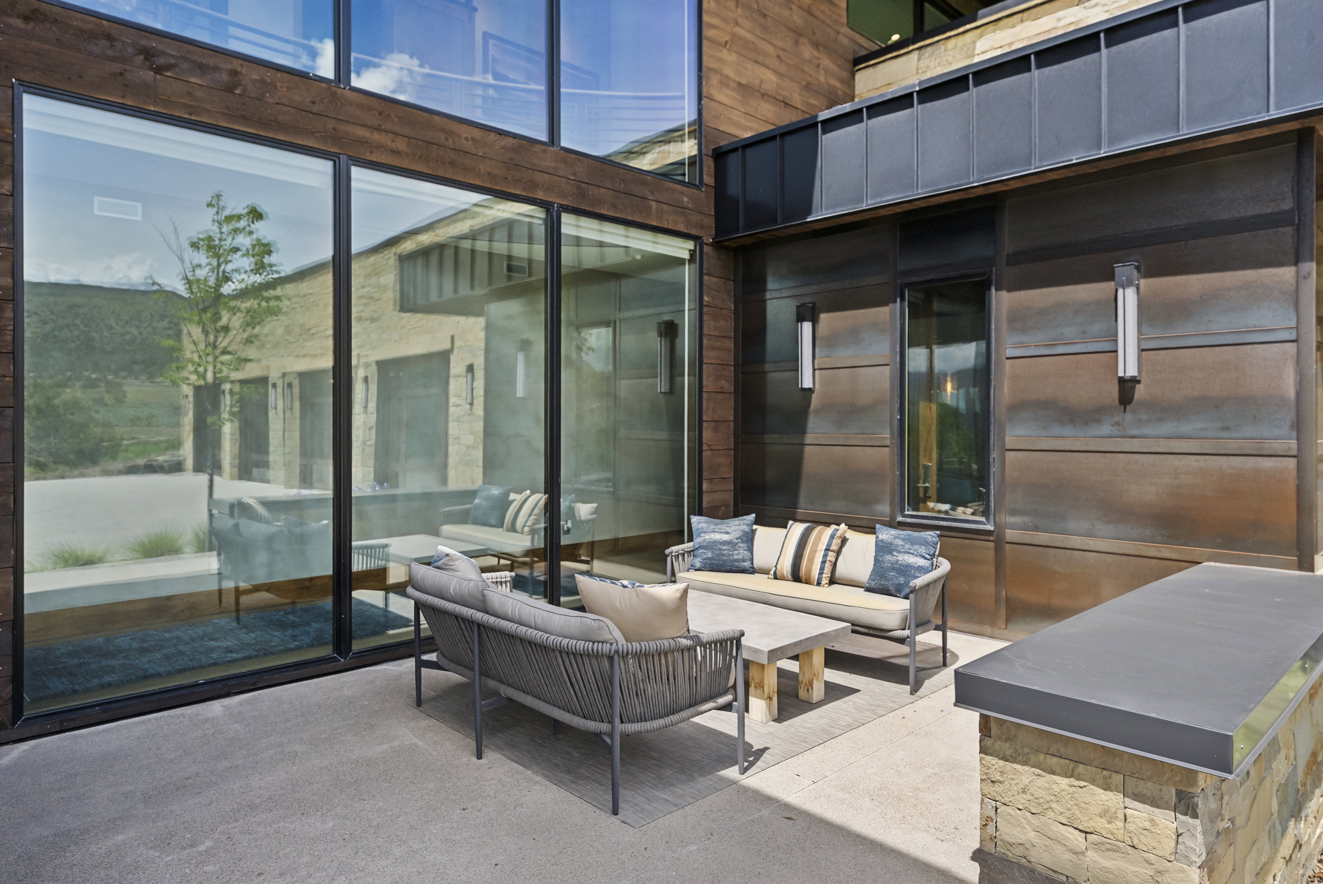 Modern outdoor patio featuring concrete flooring, a natural stone half-wall with a dark countertop, and a striking facade of wood paneling and metal siding